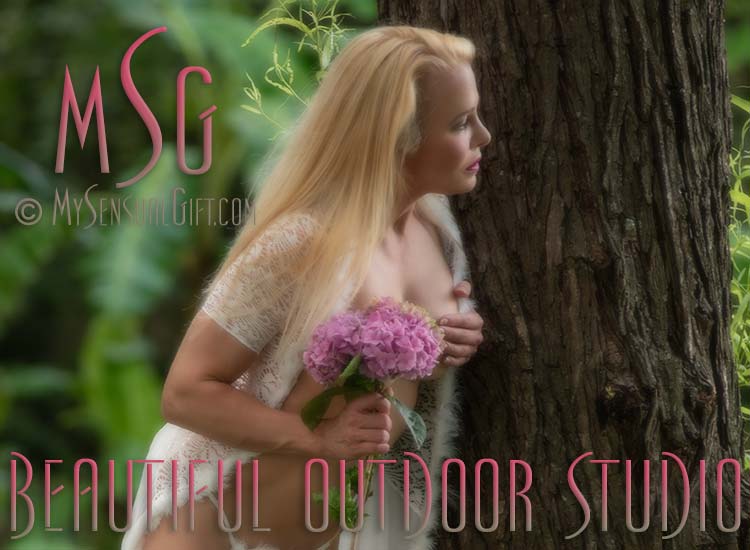 A beautiful blonde with flowers peeking around a tree.